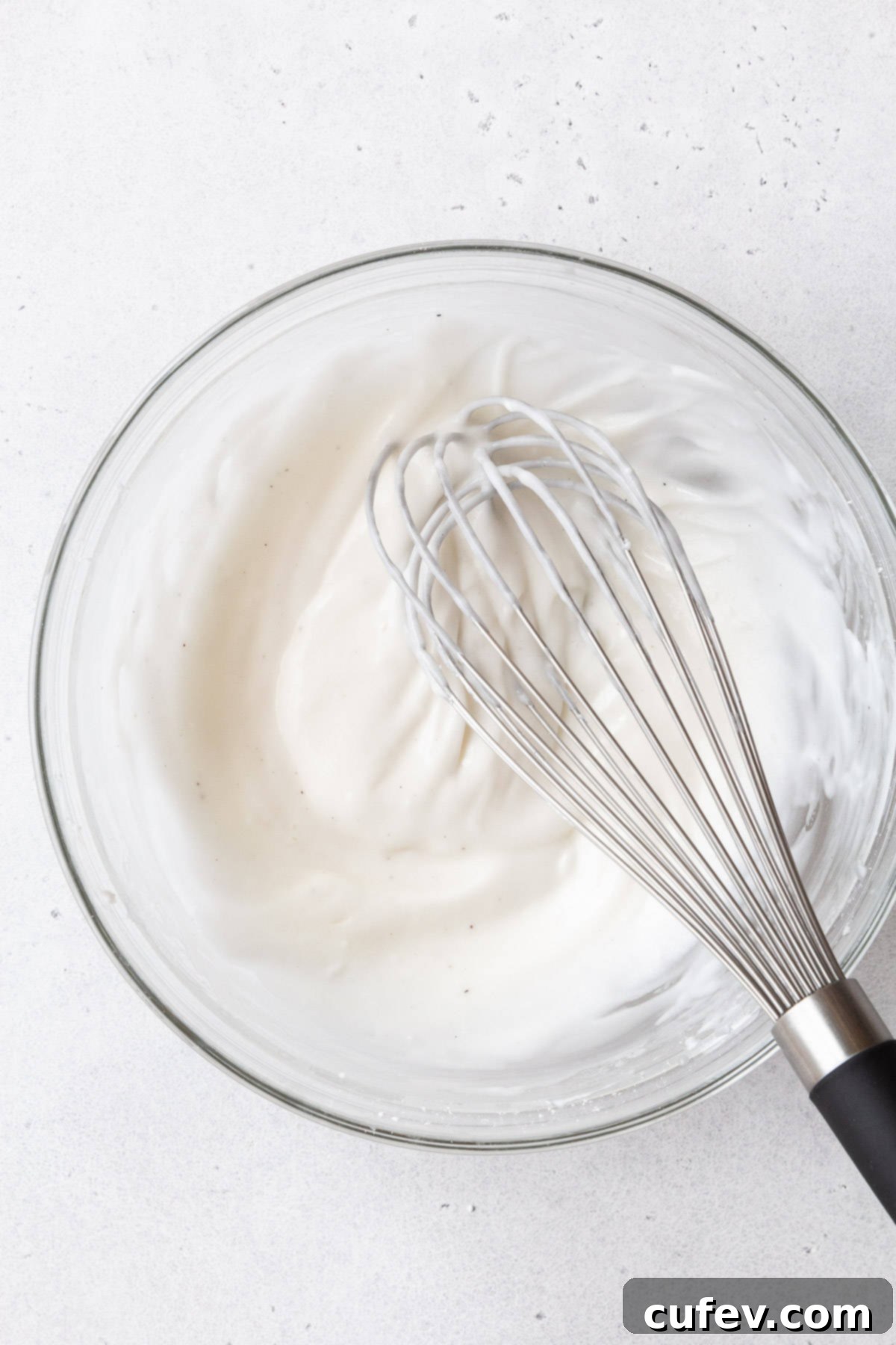 A glass mixing bowl of the cream cheese glaze with a whisk.