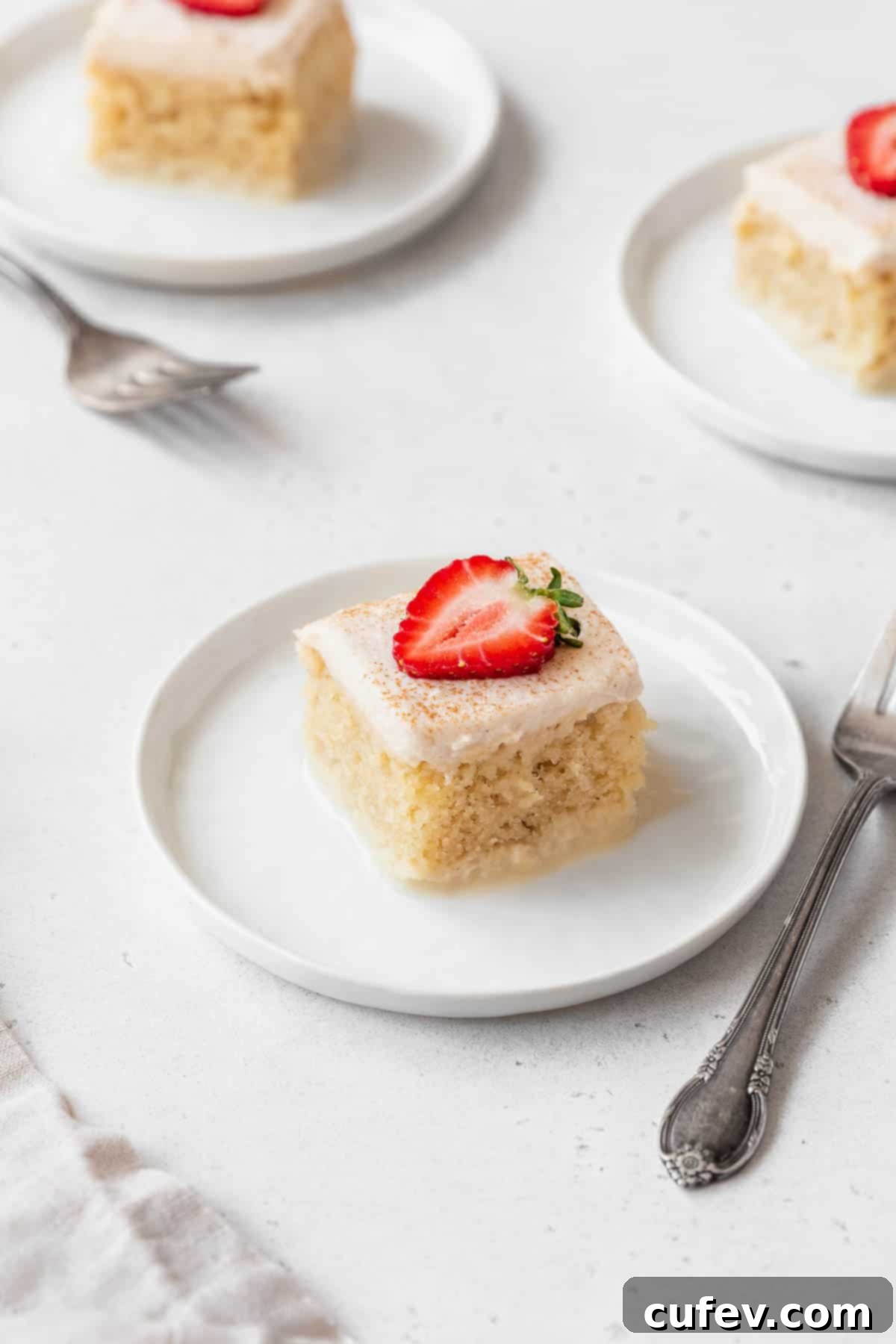 Indulgent Gluten-Free and Dairy-Free Tres Leches Cake 2 Three slices of gluten-free tres leches cake on white dessert plates with strawberries.