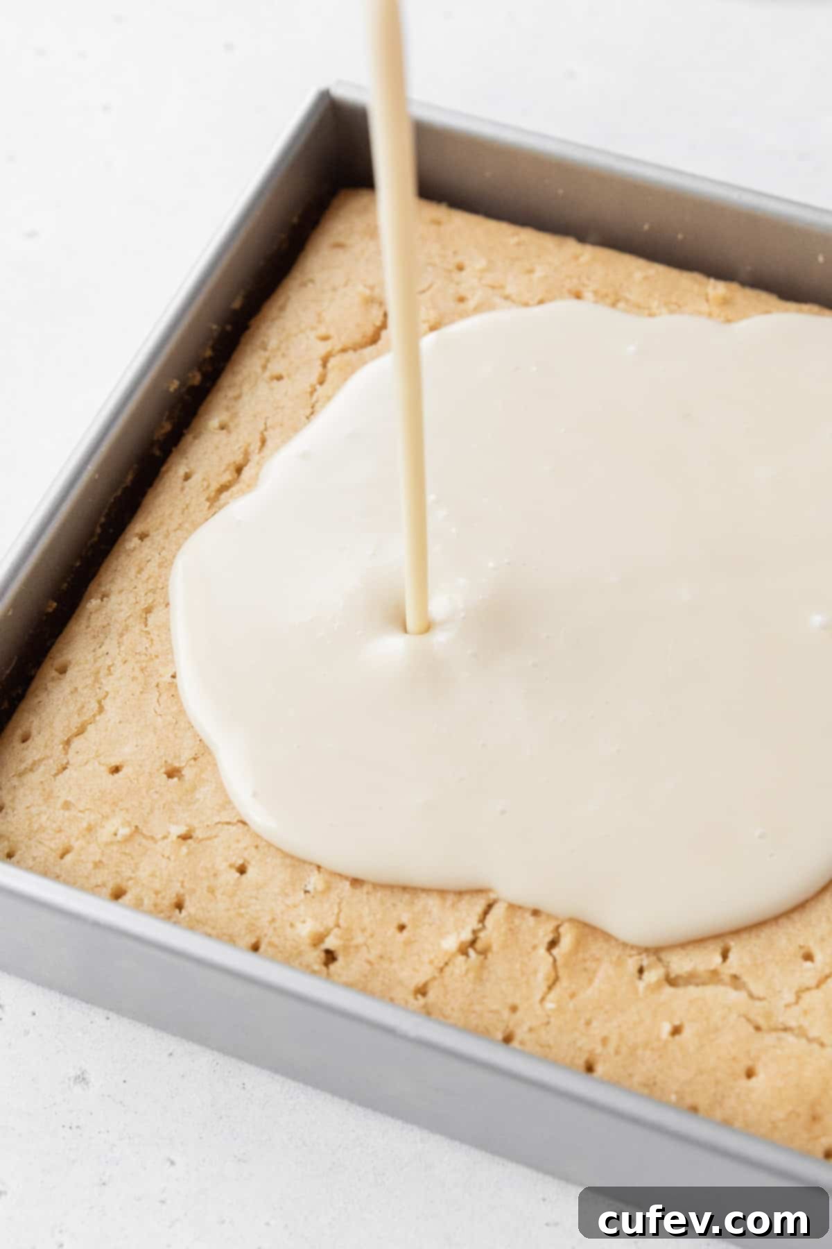 Indulgent Gluten-Free and Dairy-Free Tres Leches Cake 12 Pouring the dairy-free tres leches milk soak over the cake with poked holes in it.