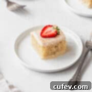Indulgent Gluten-Free and Dairy-Free Tres Leches Cake 17 A square shot of a slice of gluten-free tres leches cake on a white dessert plate with a slice of strawberry on top.