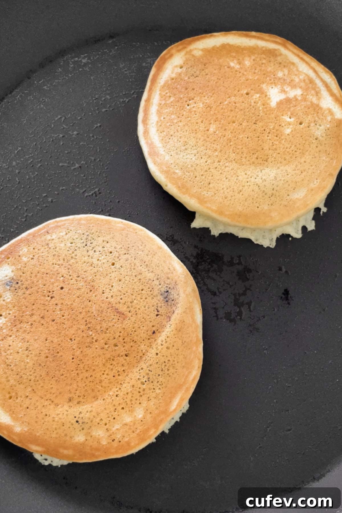 A process shot showcasing golden muffin mix pancakes after being flipped in the skillet, ready to finish cooking.