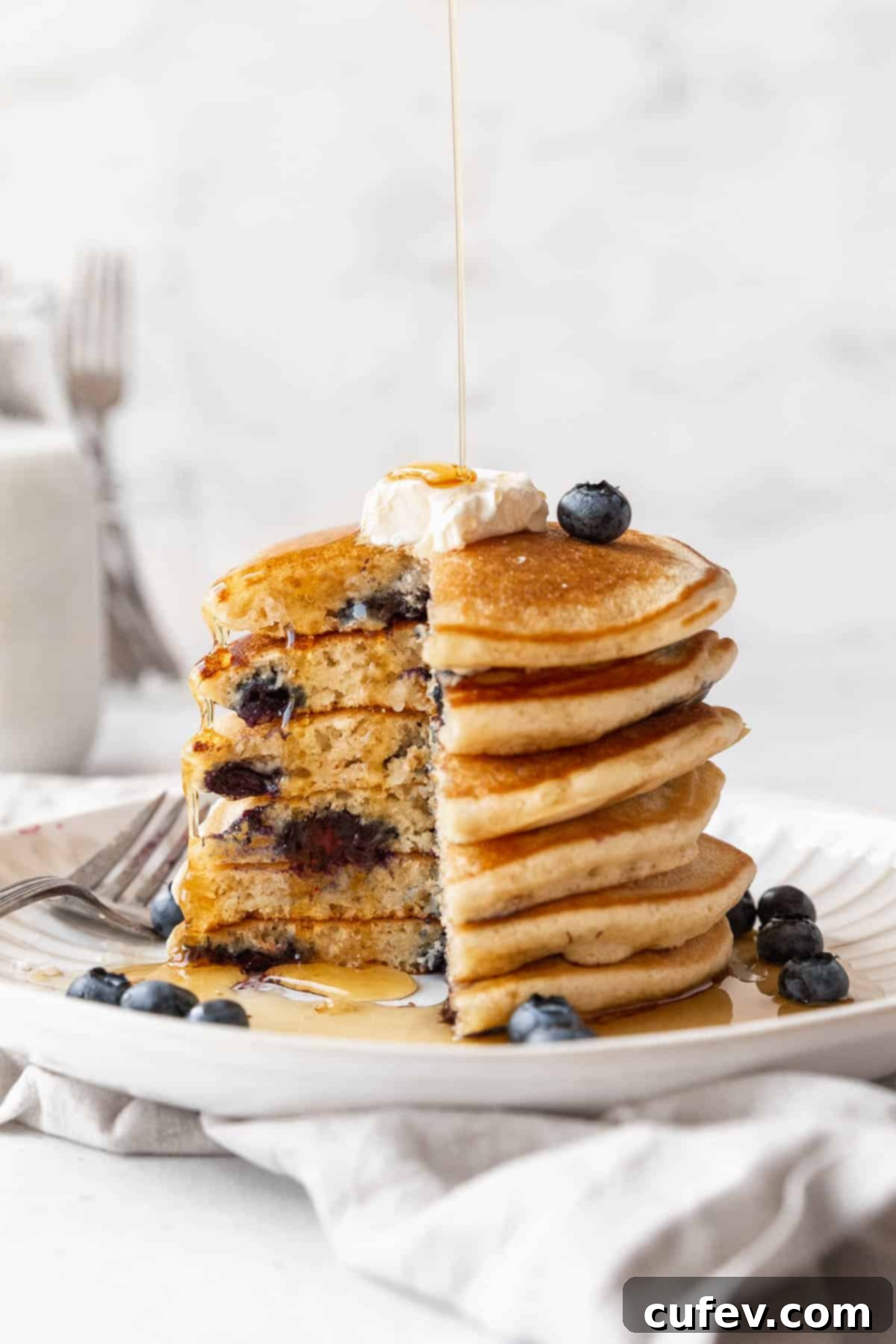 A side-on shot of a thick stack of fluffy blueberry muffin mix pancakes, with a quarter section removed to reveal the light, airy interior texture.