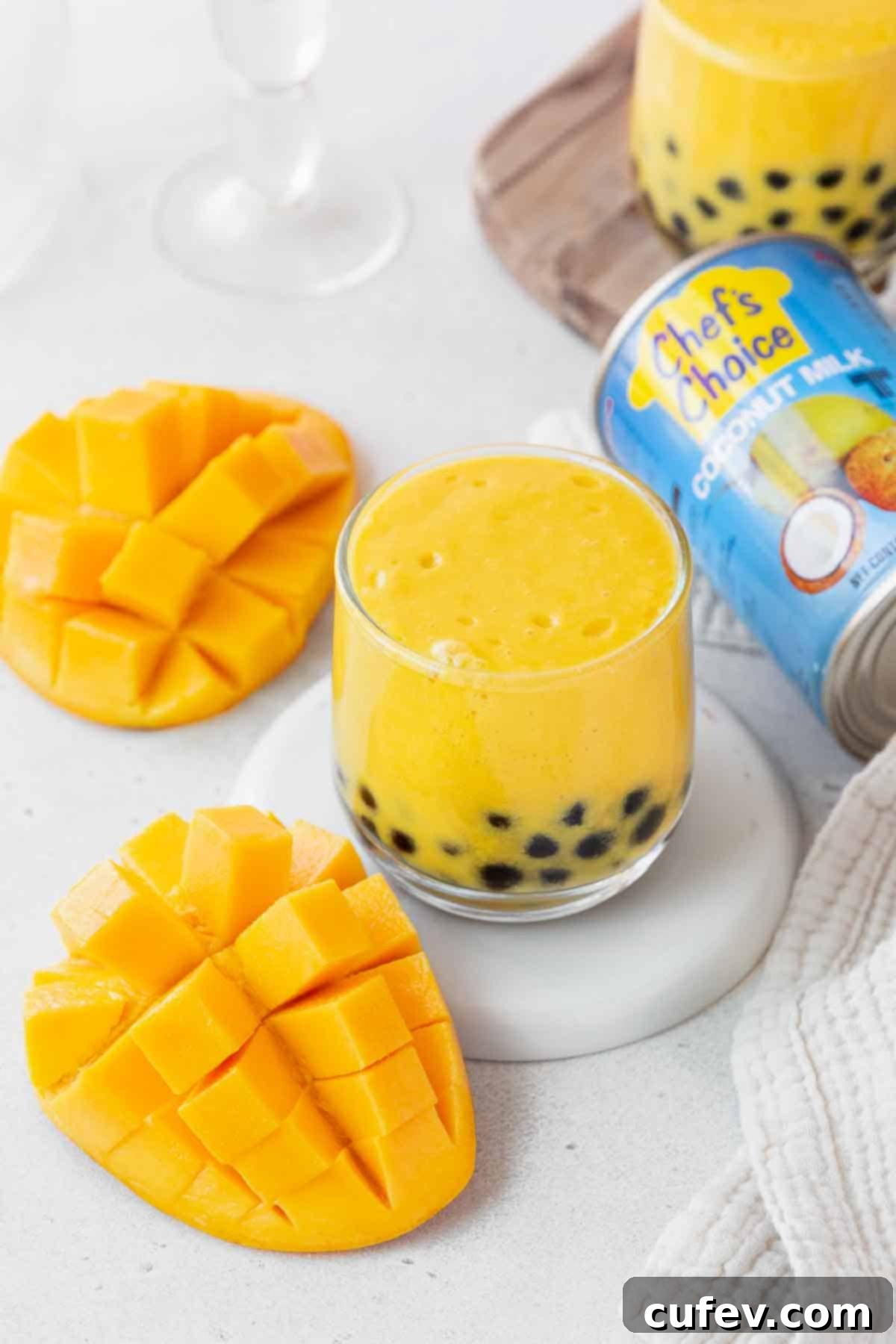 Tropical Mango Bubble Tea 13 A small glass of mango boba tea sits next to a can of Chef's Choice coconut milk and a whole cubed mango, highlighting the ingredients.