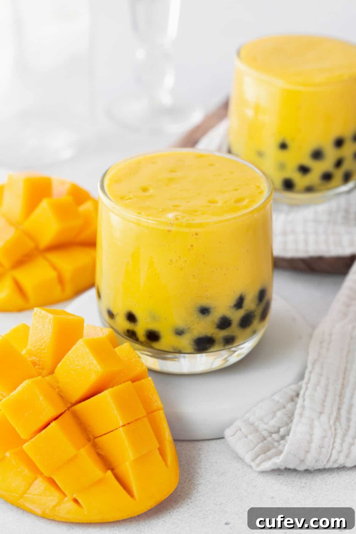 Tropical Mango Bubble Tea 14 A closeup of a small glass of mango boba tea next to a cubed mango and a white towel, highlighting the delicious drink.