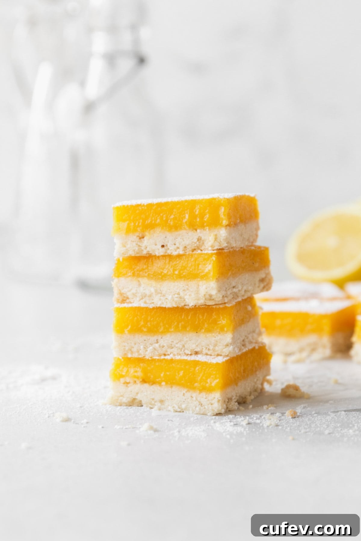 A beautiful stack of golden dairy-free lemon bars, dusted with powdered sugar, sitting invitingly on a kitchen counter.