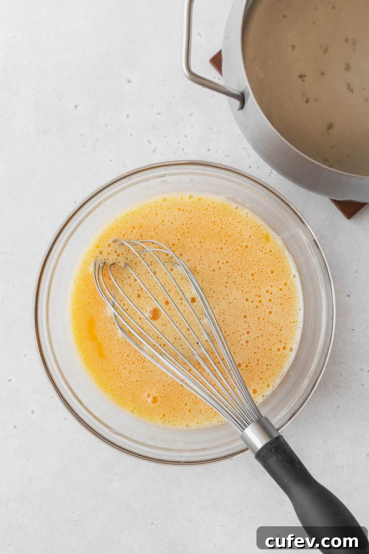 The full lemon curd mixture, now with tempered eggs, gently cooking in a saucepan on the stovetop, being continuously whisked.
