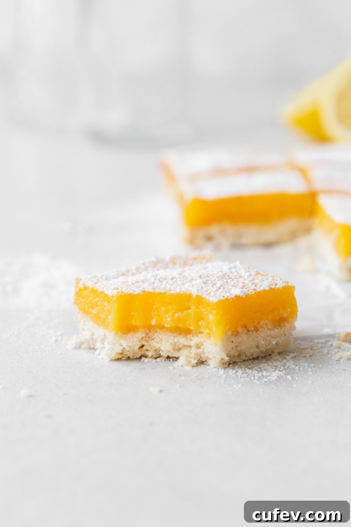 A close-up side shot of a single dairy-free lemon bar, revealing its vibrant lemon filling and tender crust, with a delicious bite taken out.