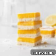 A mouth-watering image of neatly stacked dairy-free lemon bars on a counter, artfully dusted with powdered sugar and surrounded by crumbs, ready to be enjoyed.