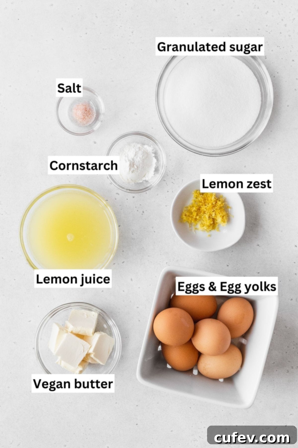 All the essential ingredients for the creamy dairy-free lemon curd filling, featuring lemons, eggs, and cornstarch, displayed on a counter.