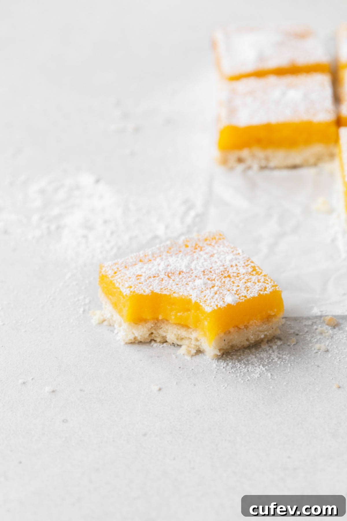 A single dairy-free lemon bar, perfectly cut and dusted with powdered sugar, with a delightful bite taken out, resting on a clean counter.