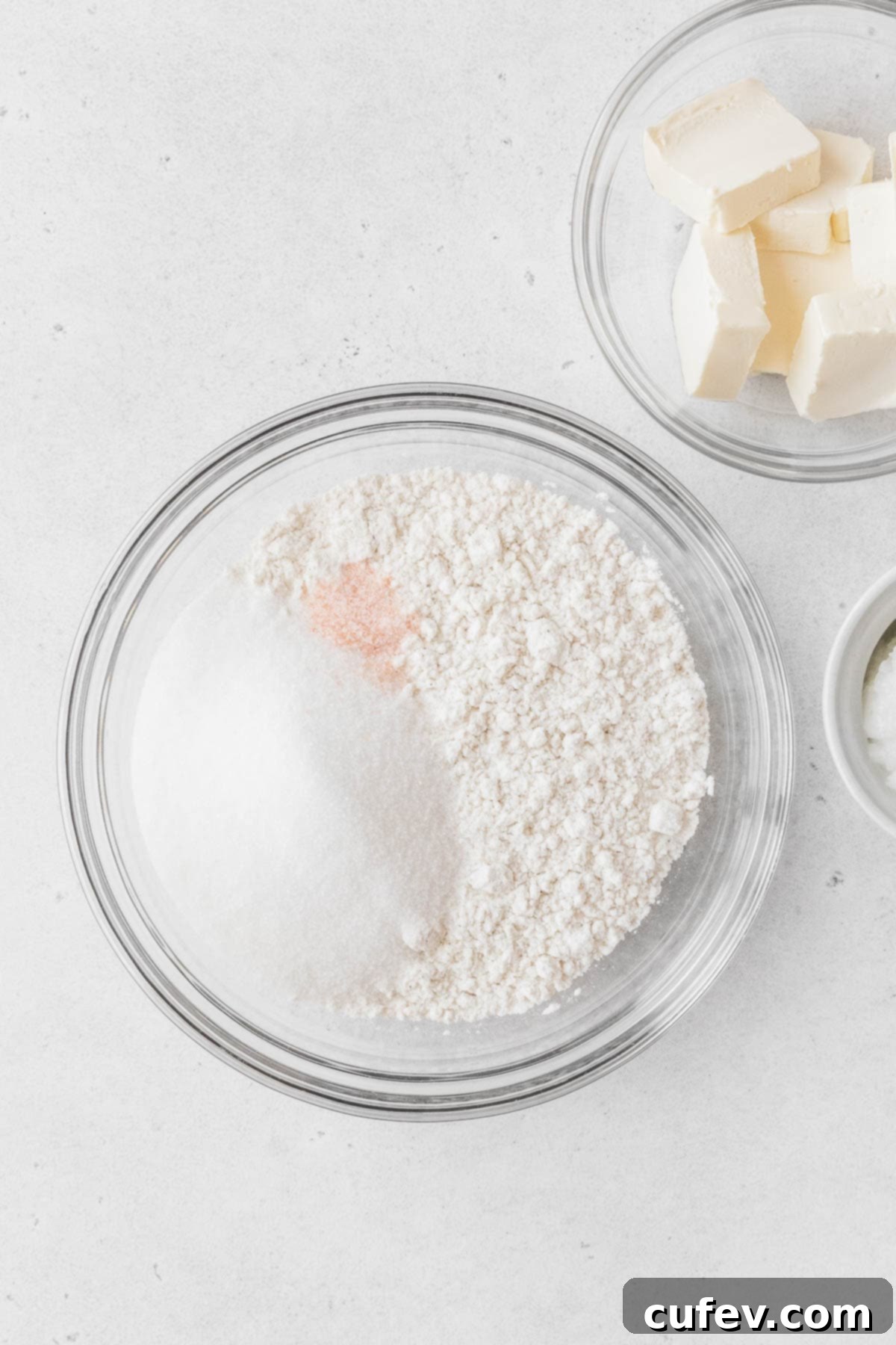 A glass mixing bowl filled with the dry ingredients—flour, sugar, and salt—ready for the addition of vegan butter.