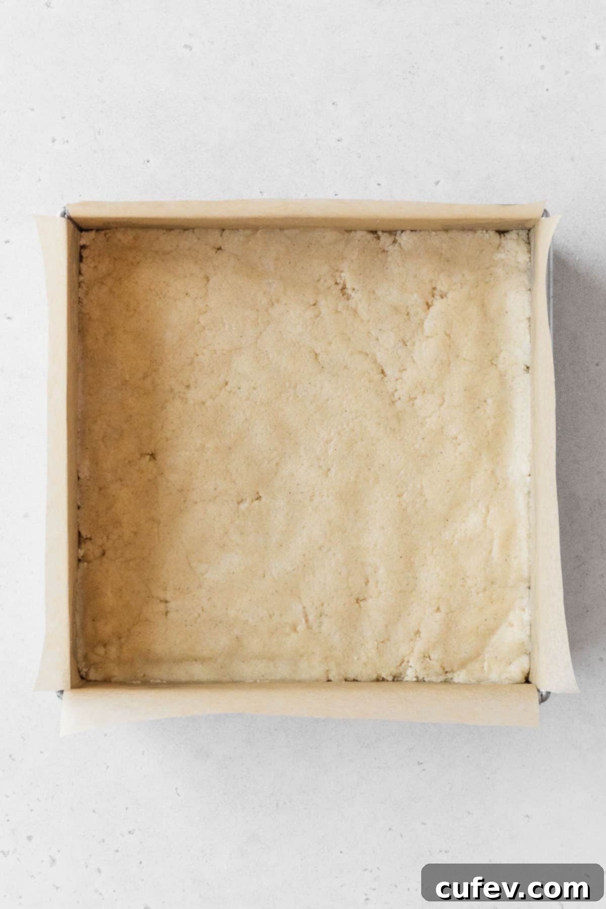 The unbaked dairy-free shortbread crust, neatly pressed into a metal baking pan lined with parchment paper.