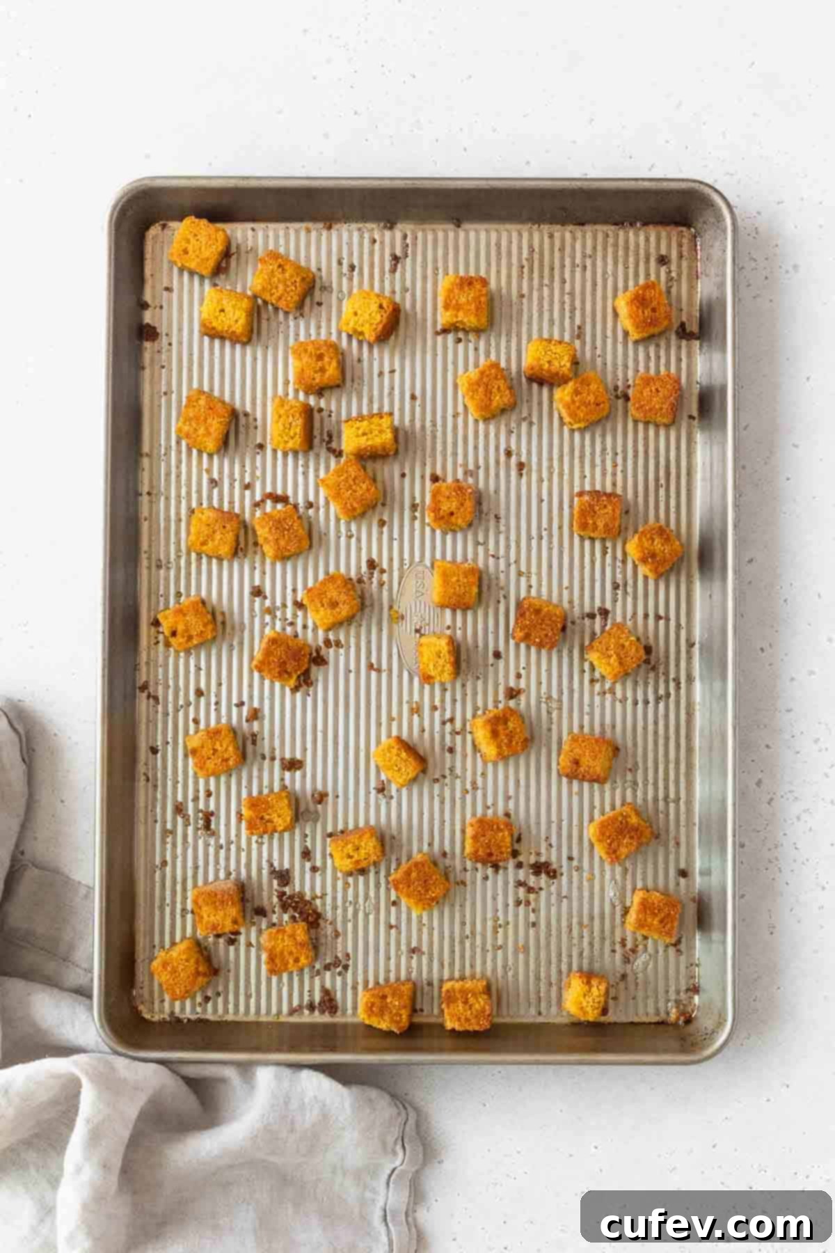 Beautifully toasted, golden-brown cornbread croutons cooling on a baking sheet after being removed from the oven, showing their perfect crisp texture.