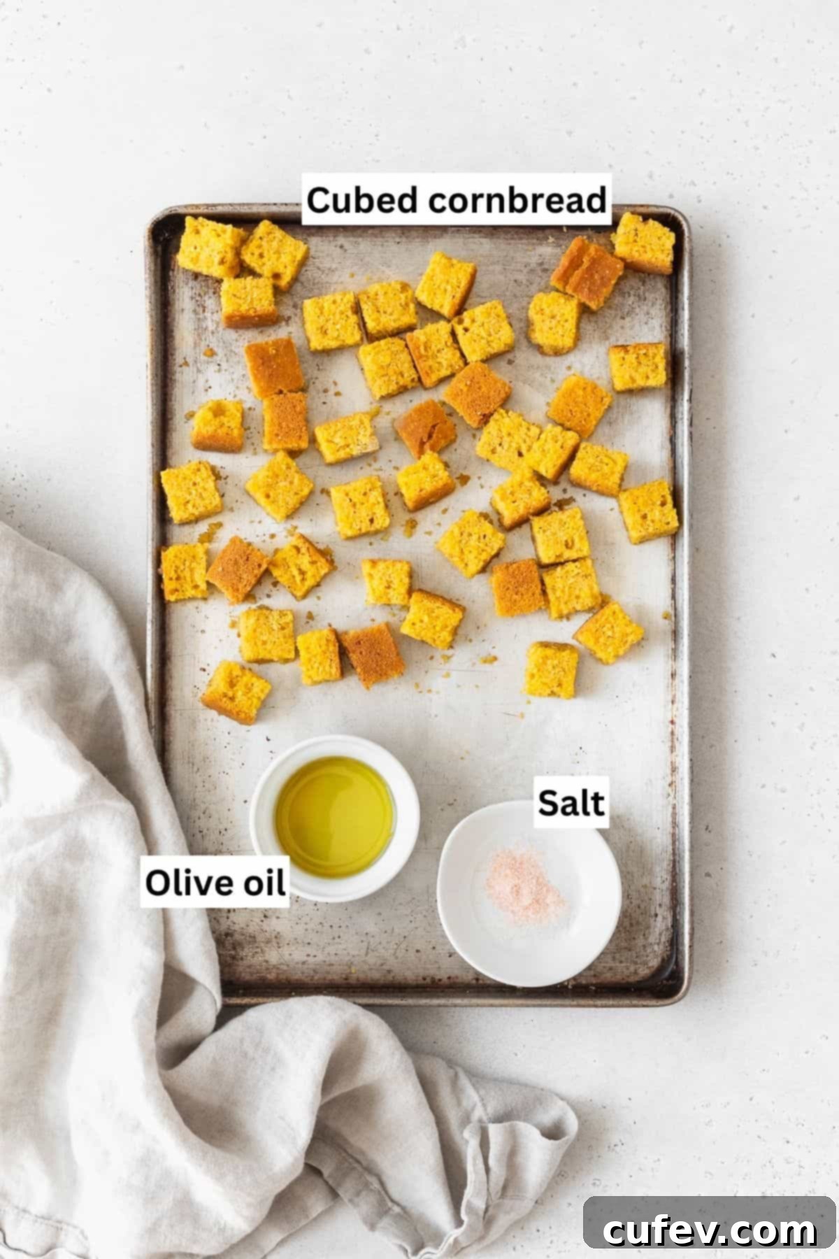 A baking sheet featuring cubed cornbread, glistening with olive oil and sprinkled with salt, prepared for baking into crispy croutons.