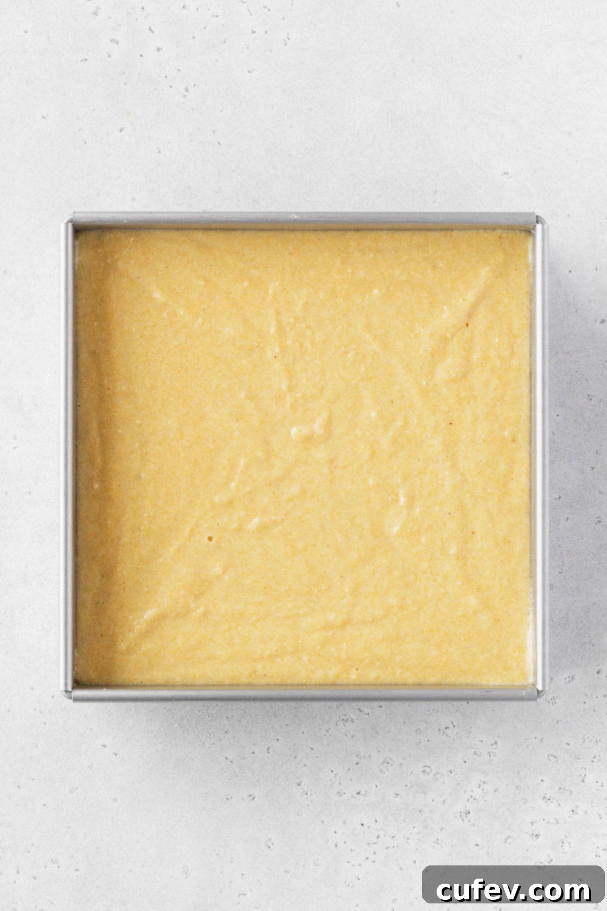 A smooth, unbaked cornbread batter poured into a square baking pan, ready to go into the oven.