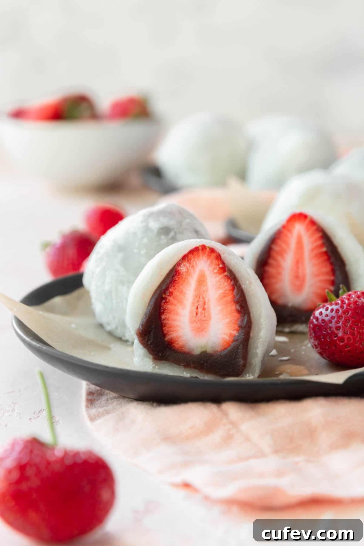 Fresh Japanese Strawberry Mochi 2 Ichigo daifuku sliced in half placed on a black plate lined with a piece of parchment paper.