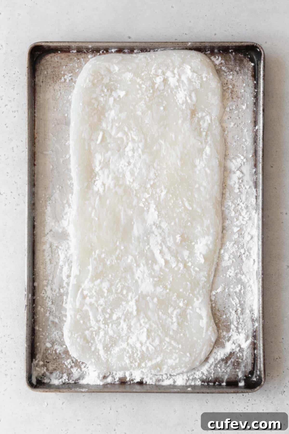 Fresh Japanese Strawberry Mochi 12 Mochi flatted out into a rectangle on a baking sheet dusted with potato starch.