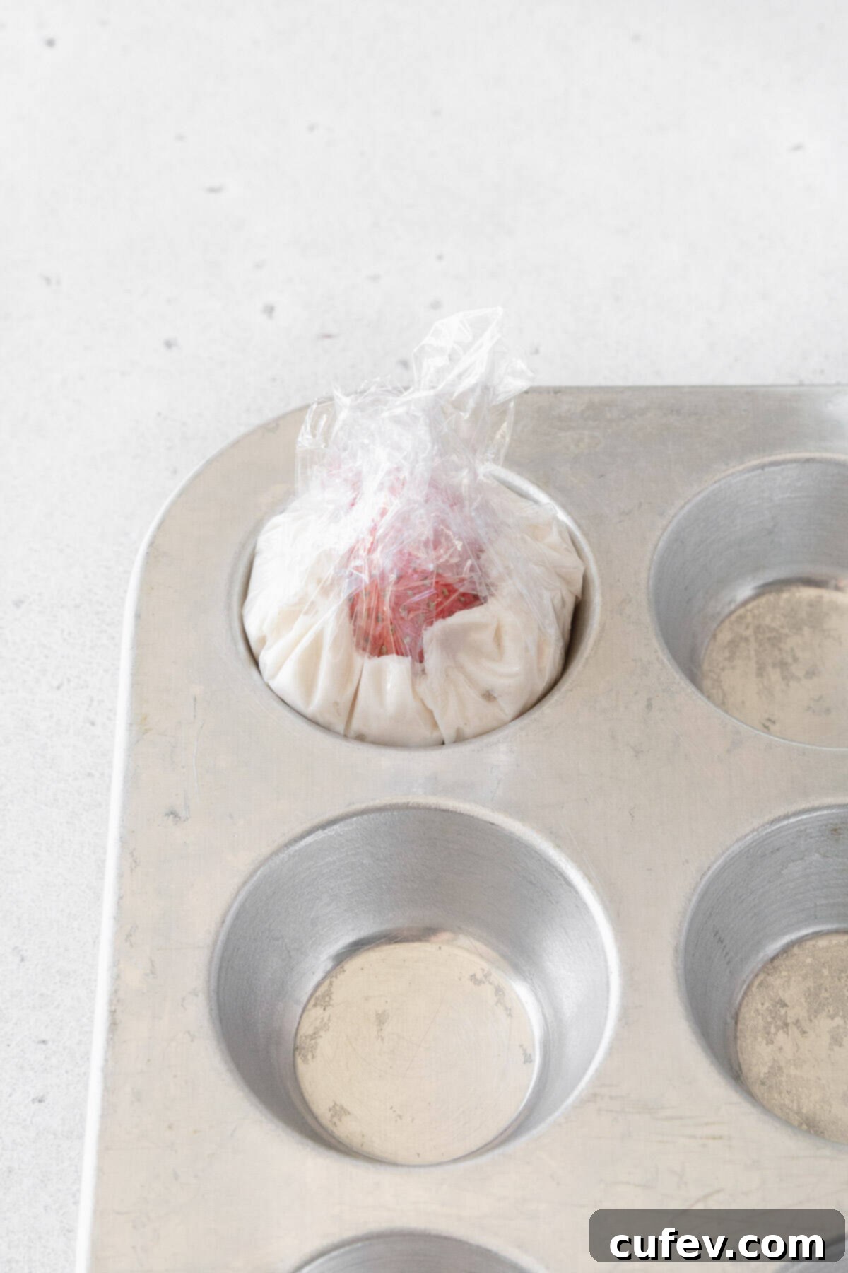 Fresh Japanese Strawberry Mochi 18 Plastic wrap twisted over a strawberry and some whipped cream in a mini muffin tin.