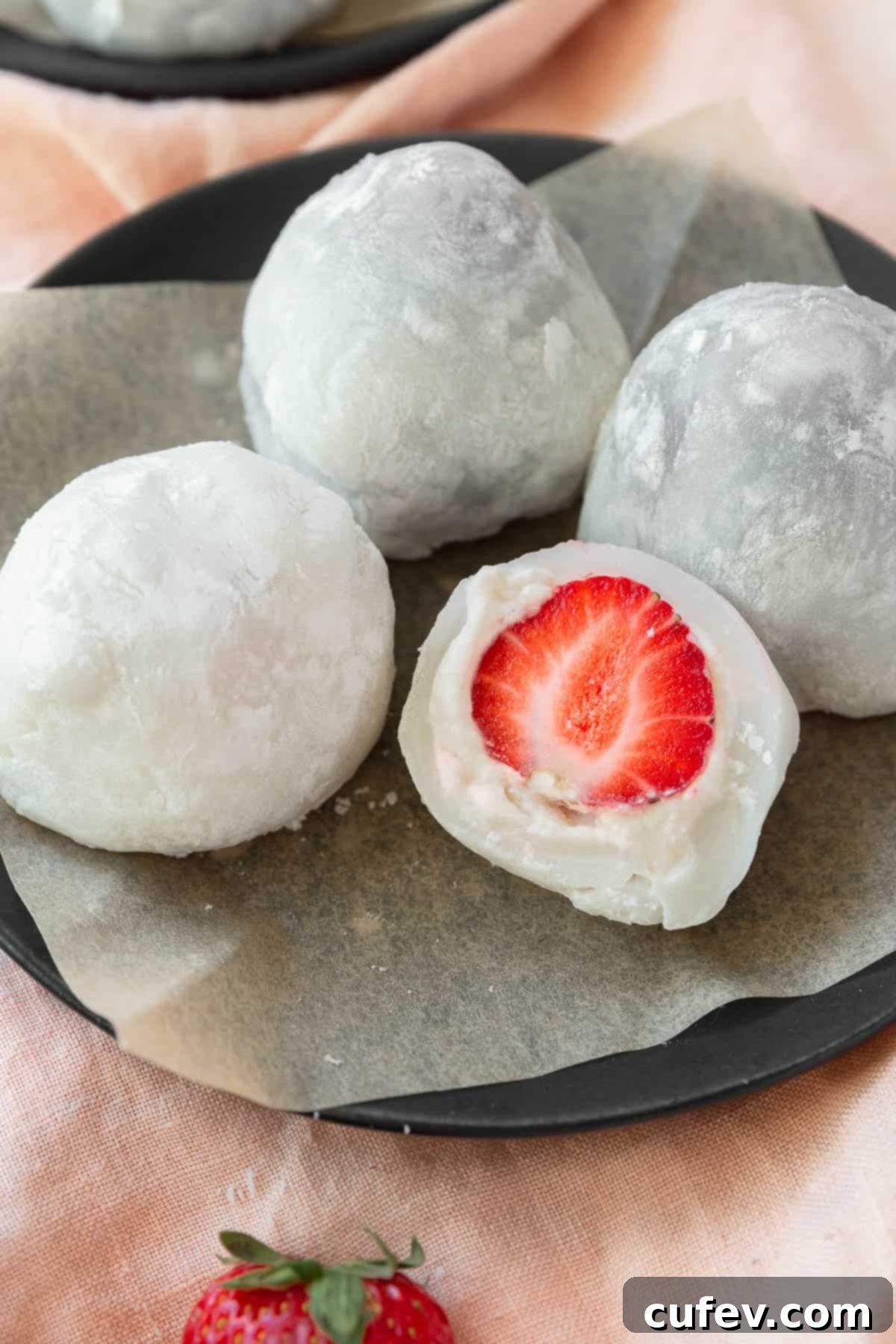 Fresh Japanese Strawberry Mochi 19 A plate of strawberry mochi with one sliced in half, filled with a strawberry and some cream.