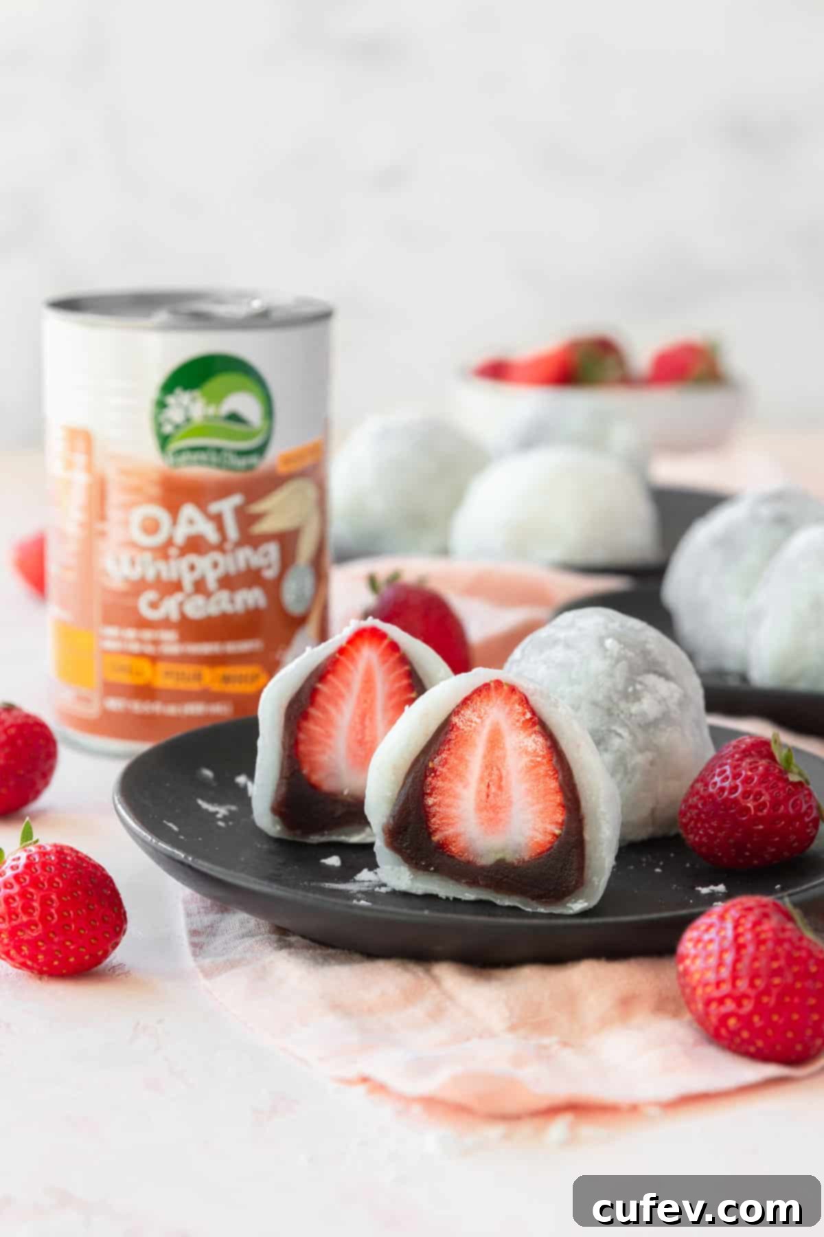 Fresh Japanese Strawberry Mochi 20 Sliced strawberry mochi on a plate with a can of oat whipping cream in the background.