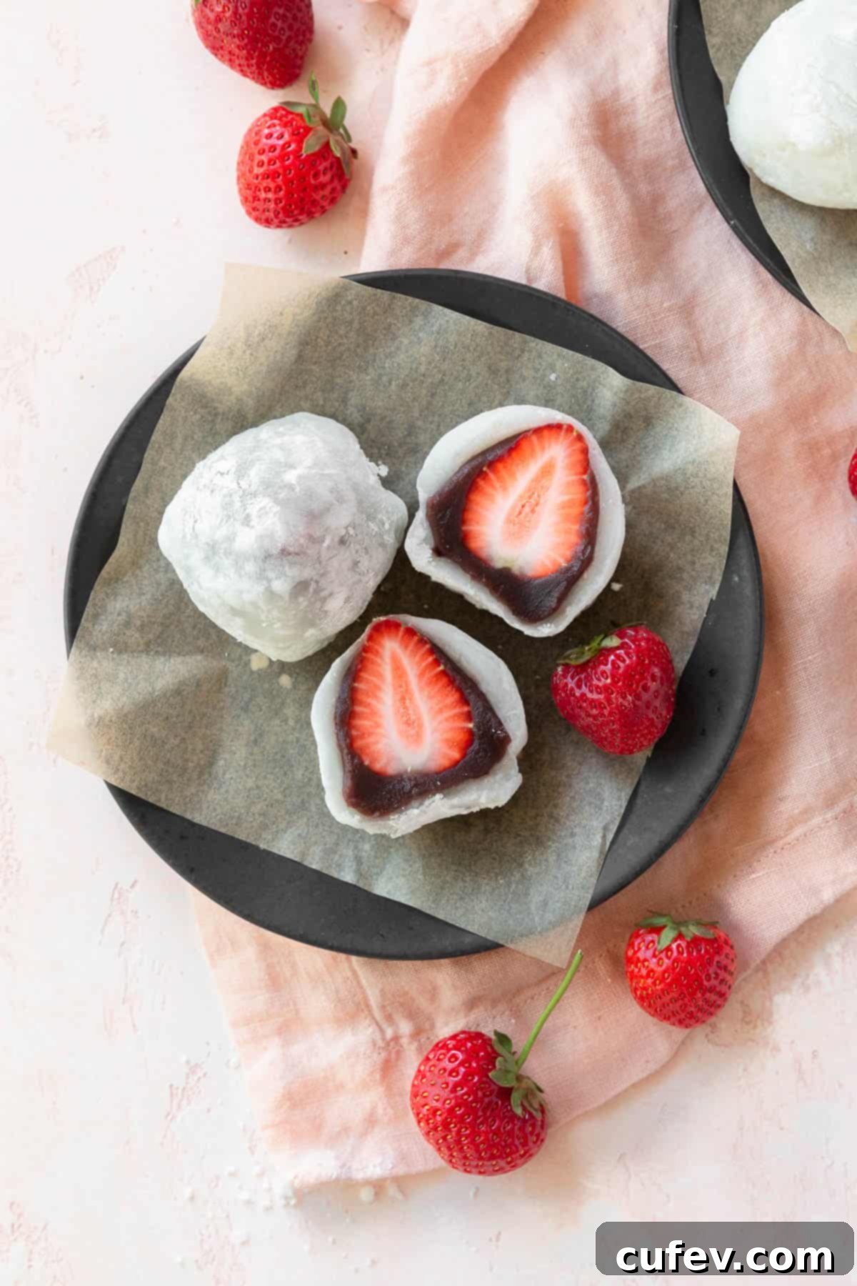 Fresh Japanese Strawberry Mochi 3 A black plate with a sliced ichigo daifuku next to a whole one.
