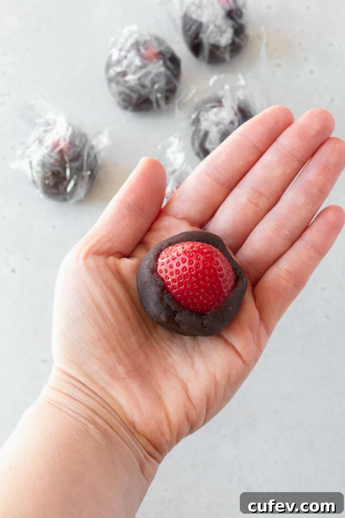 Fresh Japanese Strawberry Mochi 5 A hand holding a strawberry halfway wrapped in sweetened red bean paste.