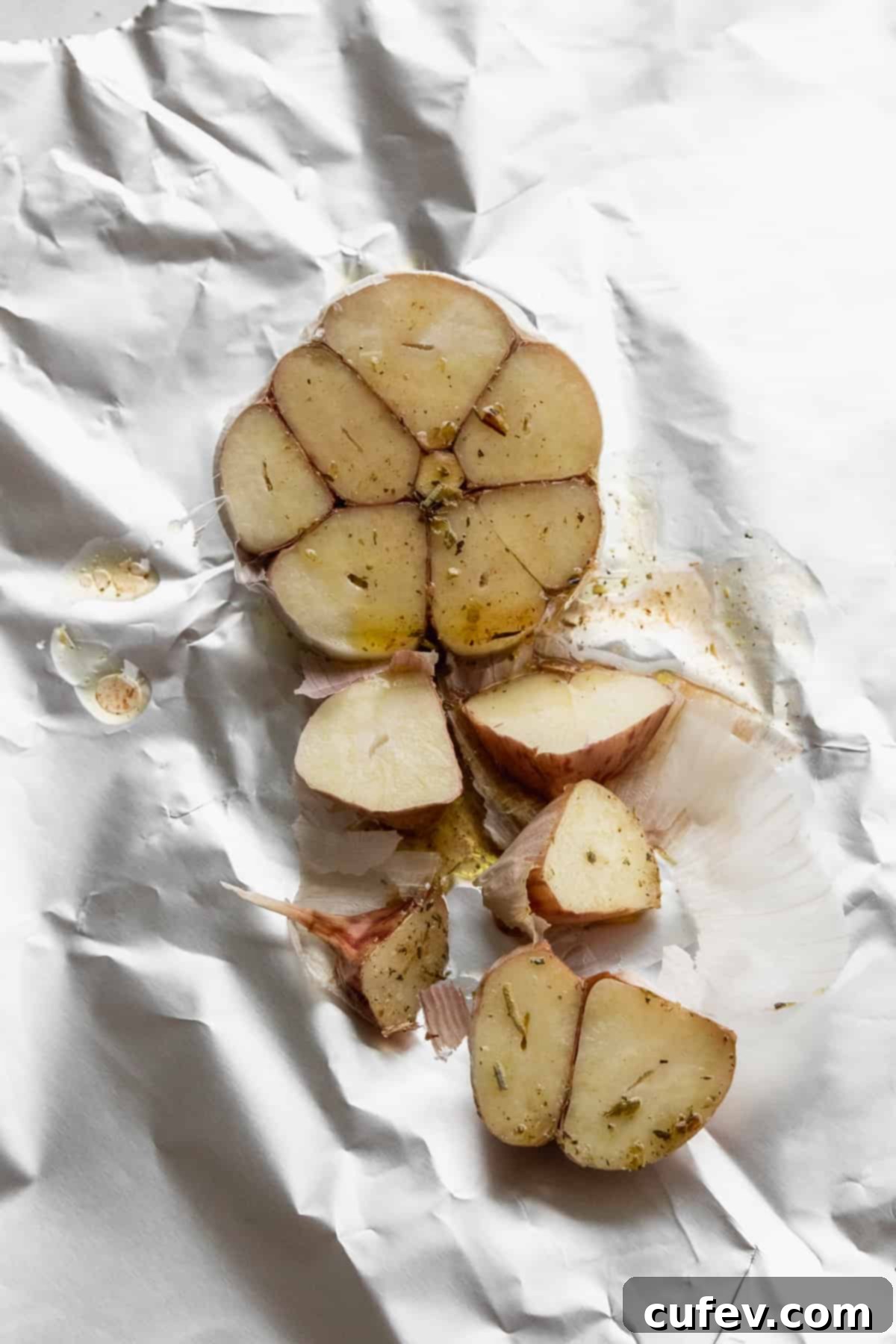 A bulb of garlic sliced in half on aluminum foil and drizzled with olive oil. 