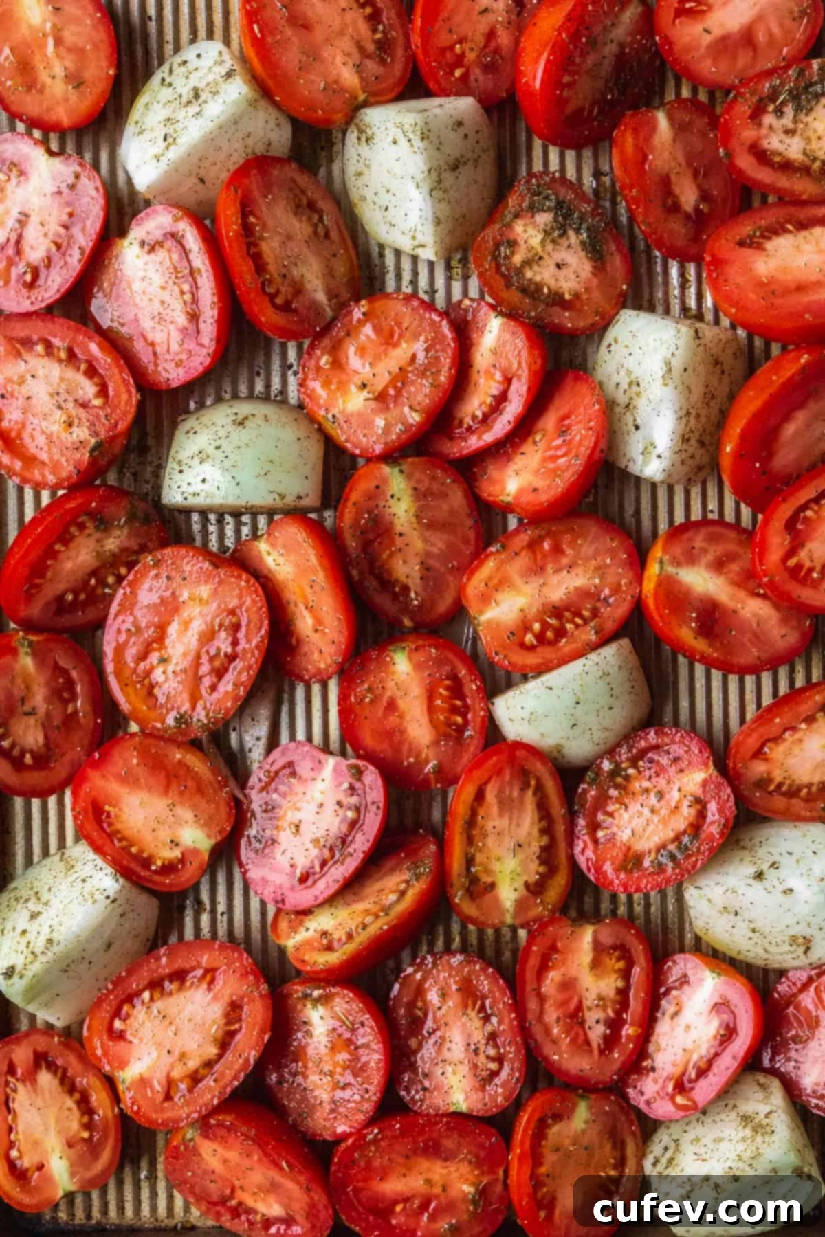 Fresh tomatoes sliced in half and chopped onions on a baking sheet.