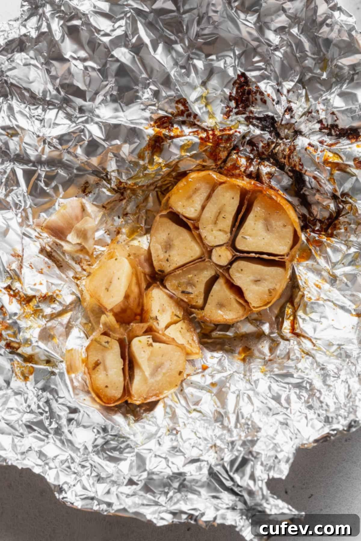 A roasted bulb of garlic on a piece of aluminum foil.