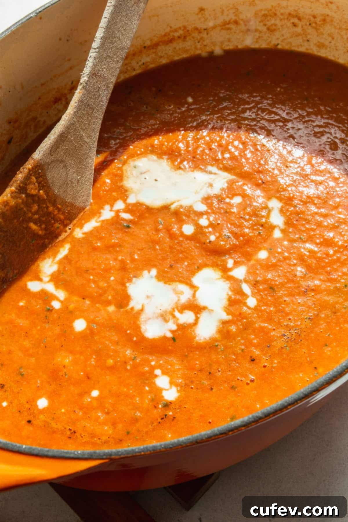 A pot of blended tomato basil soup with a swirl of coconut milk.