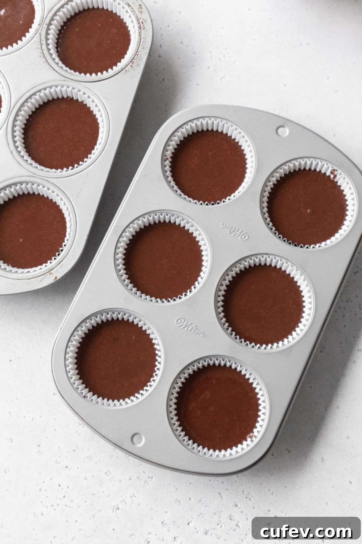 Muffin pans filled evenly with dark chocolate cupcake batter, ready to be baked to fluffy perfection.
