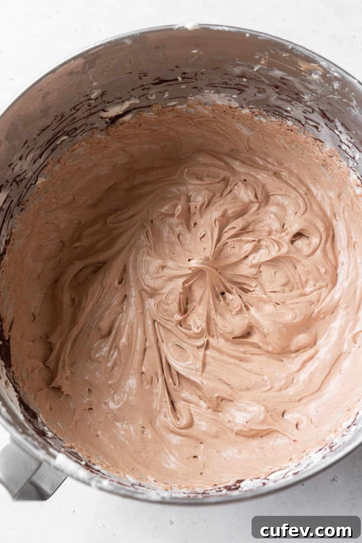 Decadent chocolate cream cheese frosting, perfectly whipped to a smooth and fluffy consistency, sitting in a gleaming metallic mixing bowl, ready to adorn freshly baked chocolate cupcakes.