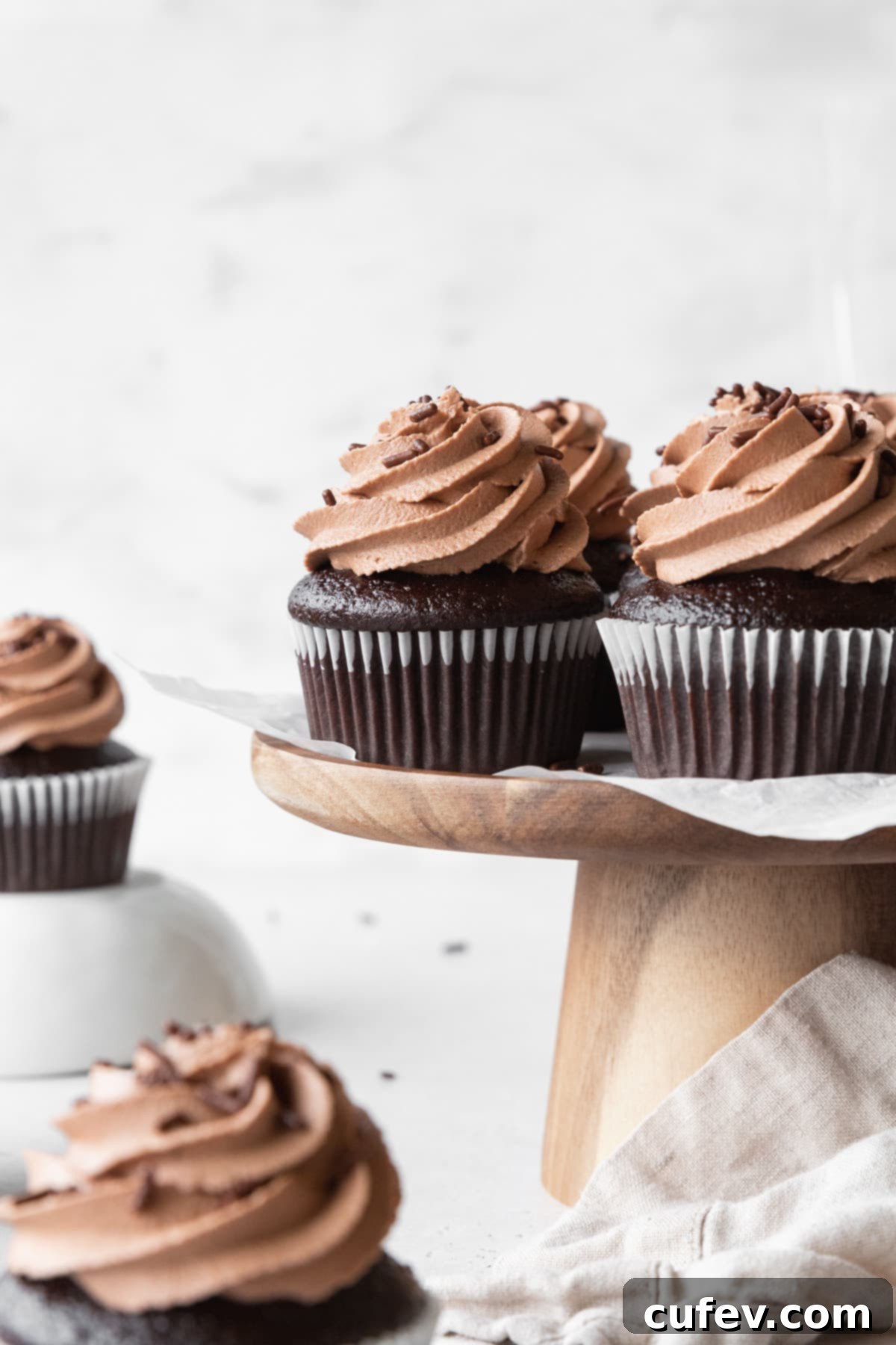 A wooden cake stand adorned with an array of moist chocolate cupcakes, generously topped with swirls of rich chocolate cream cheese frosting, inviting dessert lovers.
