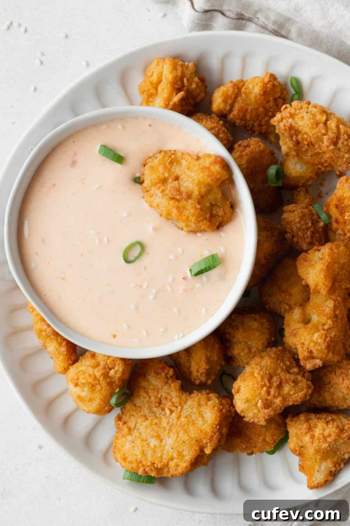 A plate of cauliflower bites with a bowl of bang bang sauce.
