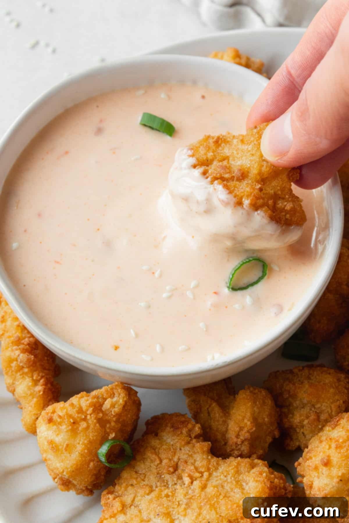 A hand holding a deep fried cauliflower and dipping it into a bowl of easy bang bang sauce.