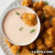 A deep fried cauliflower being dipped into a bowl of bang bang sauce.