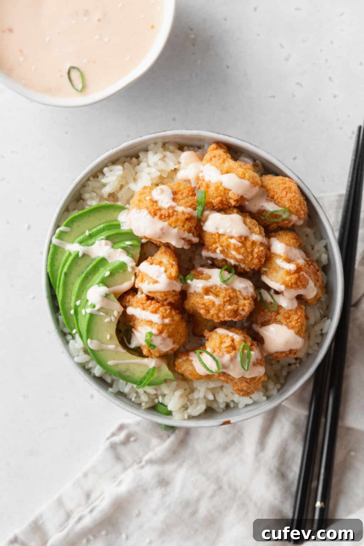 A bowl of coconut rice with bang bang cauliflower and avocado on top.