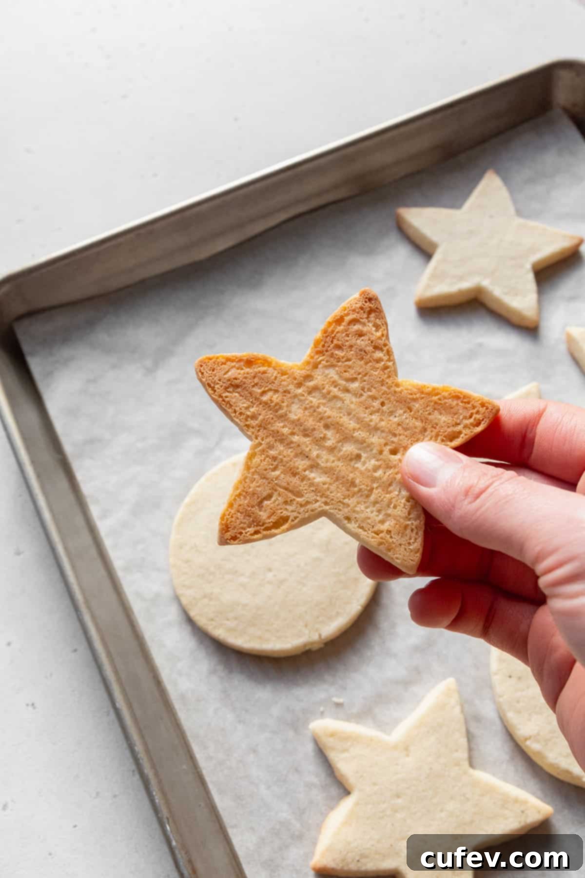 A hand holding a star-shaped sugar cookie, showing the golden color of the bottom of the cookie.