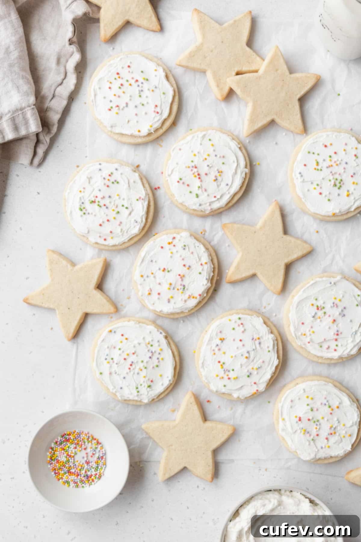Star shaped sugar cookies and round frosted gluten free cookies laid out on a white surface.