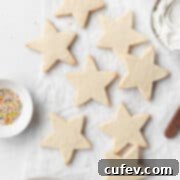 Star shaped gluten free sugar cookies on a white surface next to a small dish of sprinkles and a bowl of frosting.