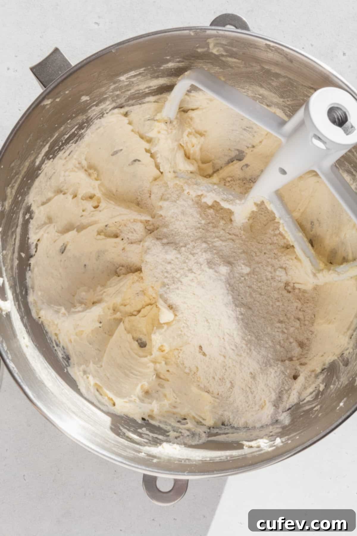 Dry ingredients added to the wet ingredients for sugar cookies in a metal bowl.