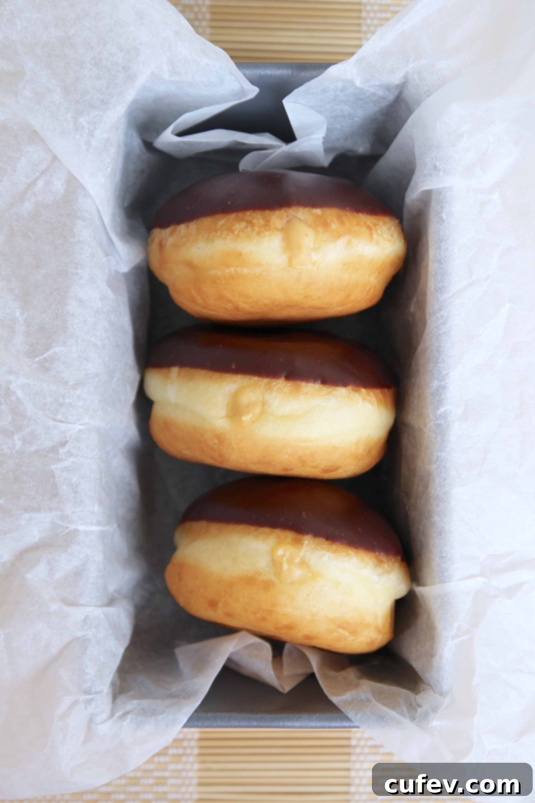 Three fluffy homemade Baileys Boston Cream Doughnuts with rich chocolate glaze and creamy Baileys custard filling in a loaf pan, ready to be enjoyed.