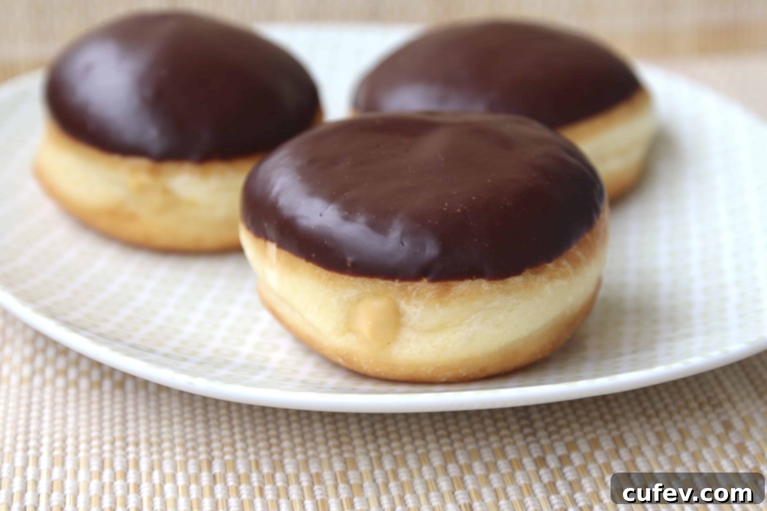 Two Baileys Boston Cream Doughnuts arranged beautifully on a white plate, showcasing their rich chocolate glaze and fluffy texture, inviting a taste.
