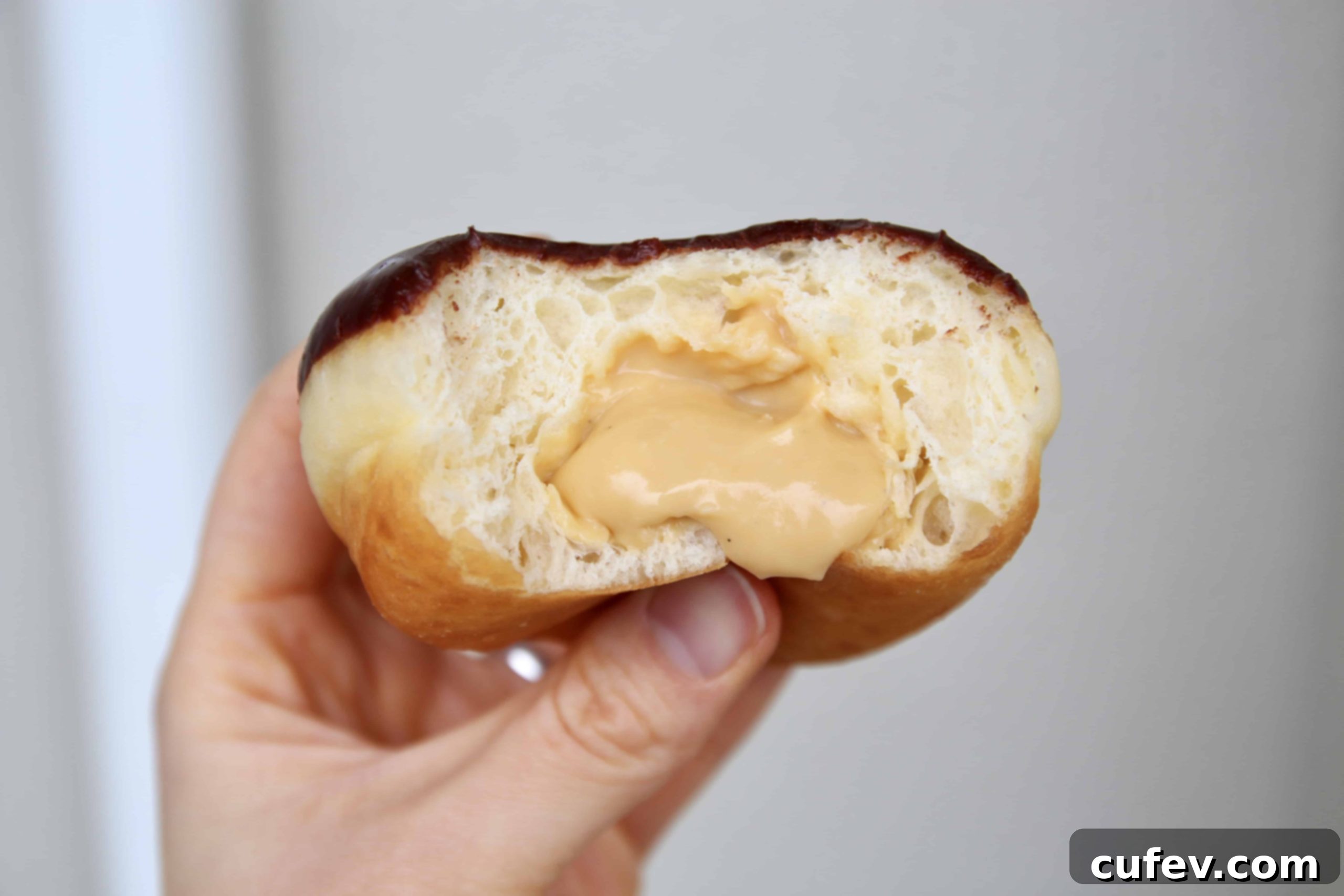A delicious Baileys Boston Cream Doughnut bitten into, revealing its creamy Baileys custard filling and rich dark chocolate glaze, highlighting the layers of flavor.