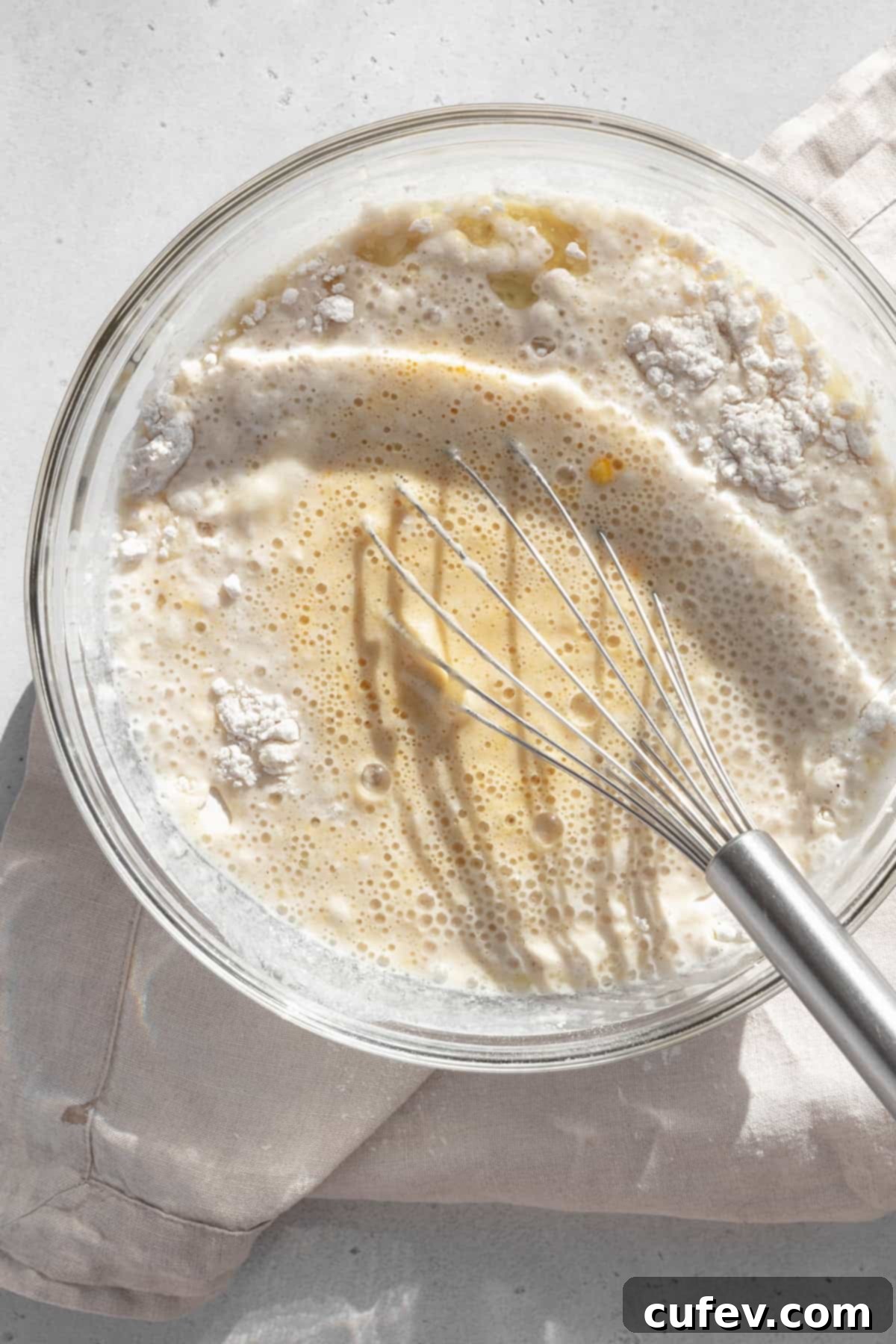 Gluten-free waffle batter is being gently whisked in a clear glass bowl, showcasing the mixing process before cooking.