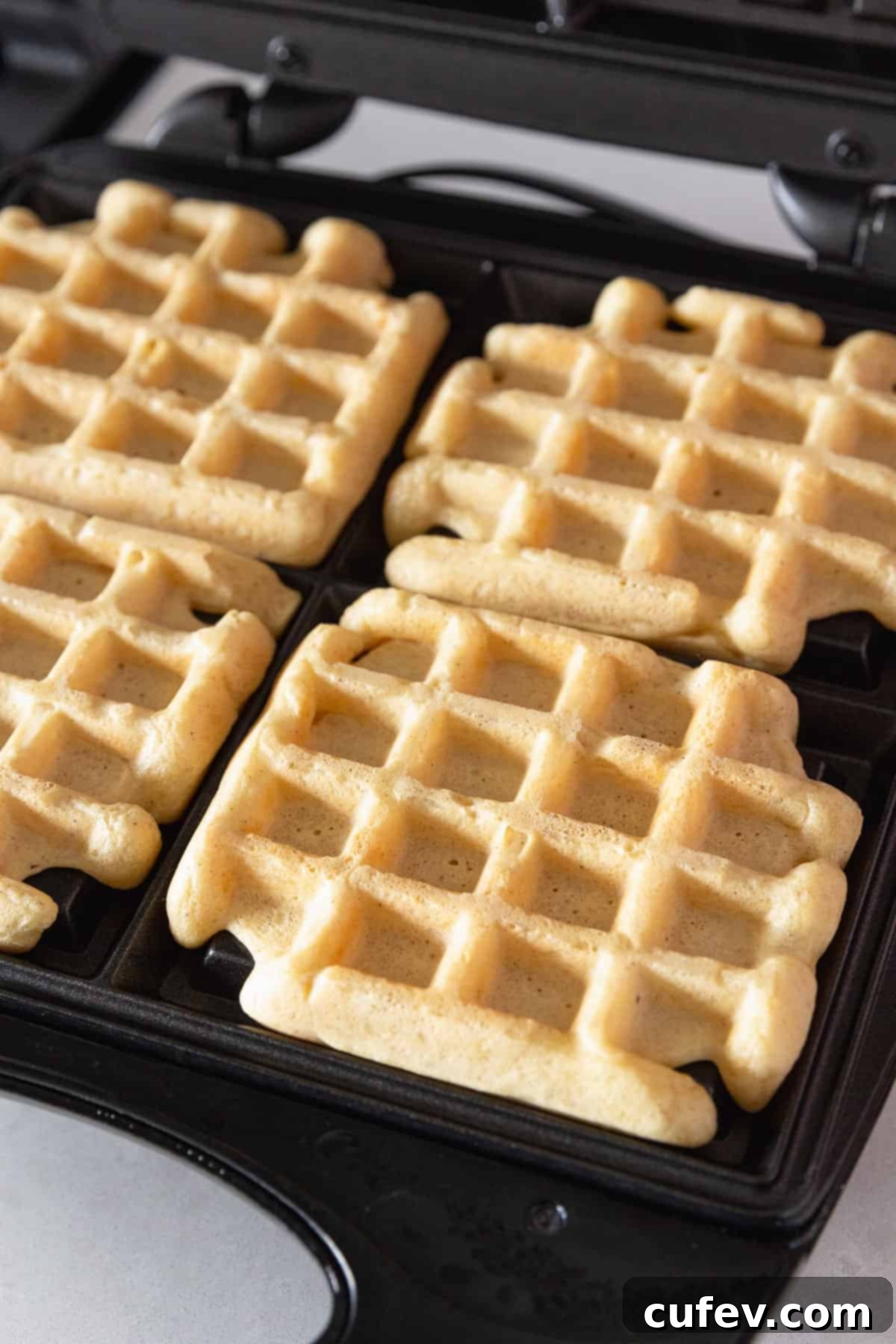 A freshly cooked gluten-free waffle, golden and perfectly shaped, is shown resting on a hot waffle iron, steam gently rising.