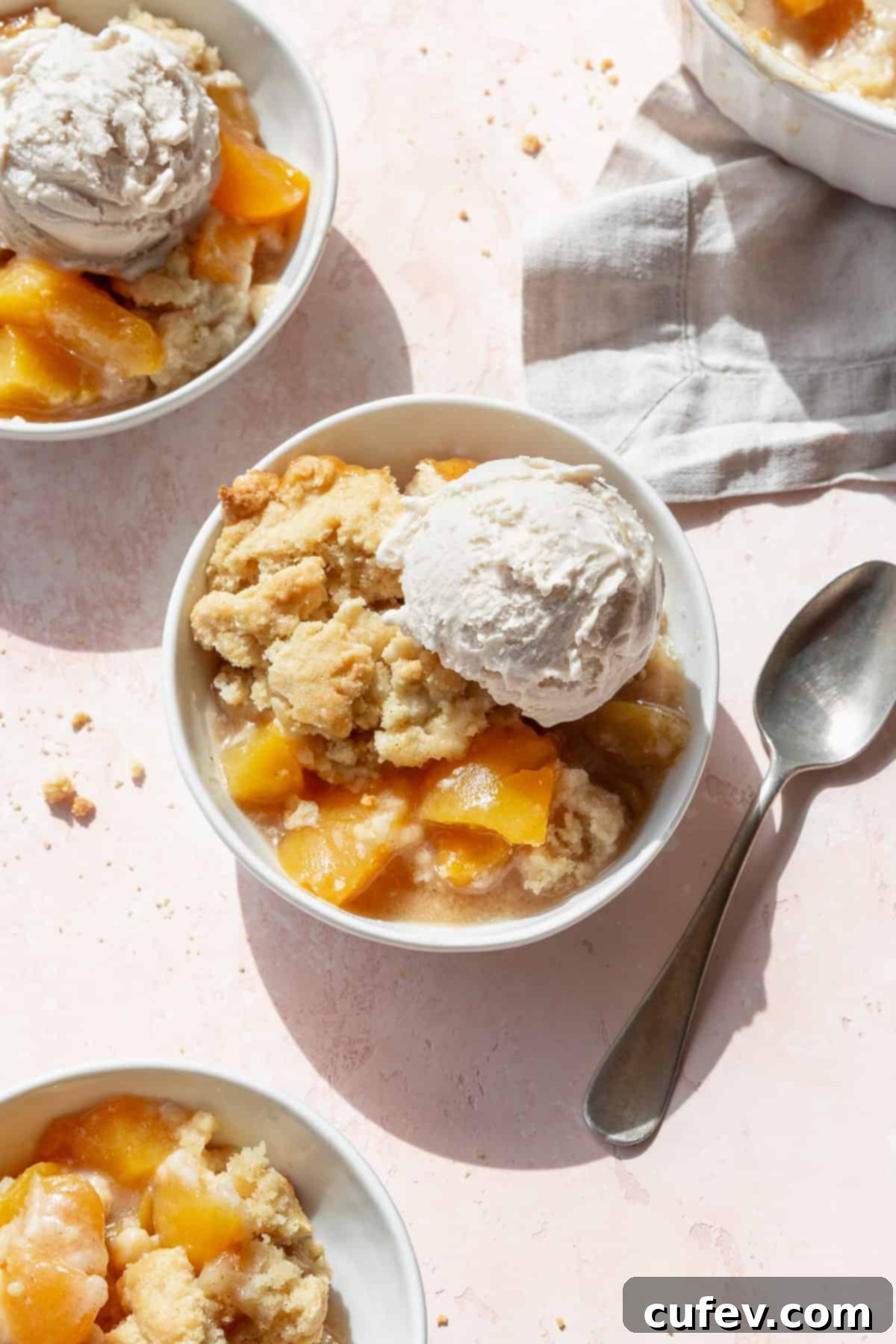Overhead shot of peach cobbler with canned peaches in three white bowls with scoops of vanilla ice cream.