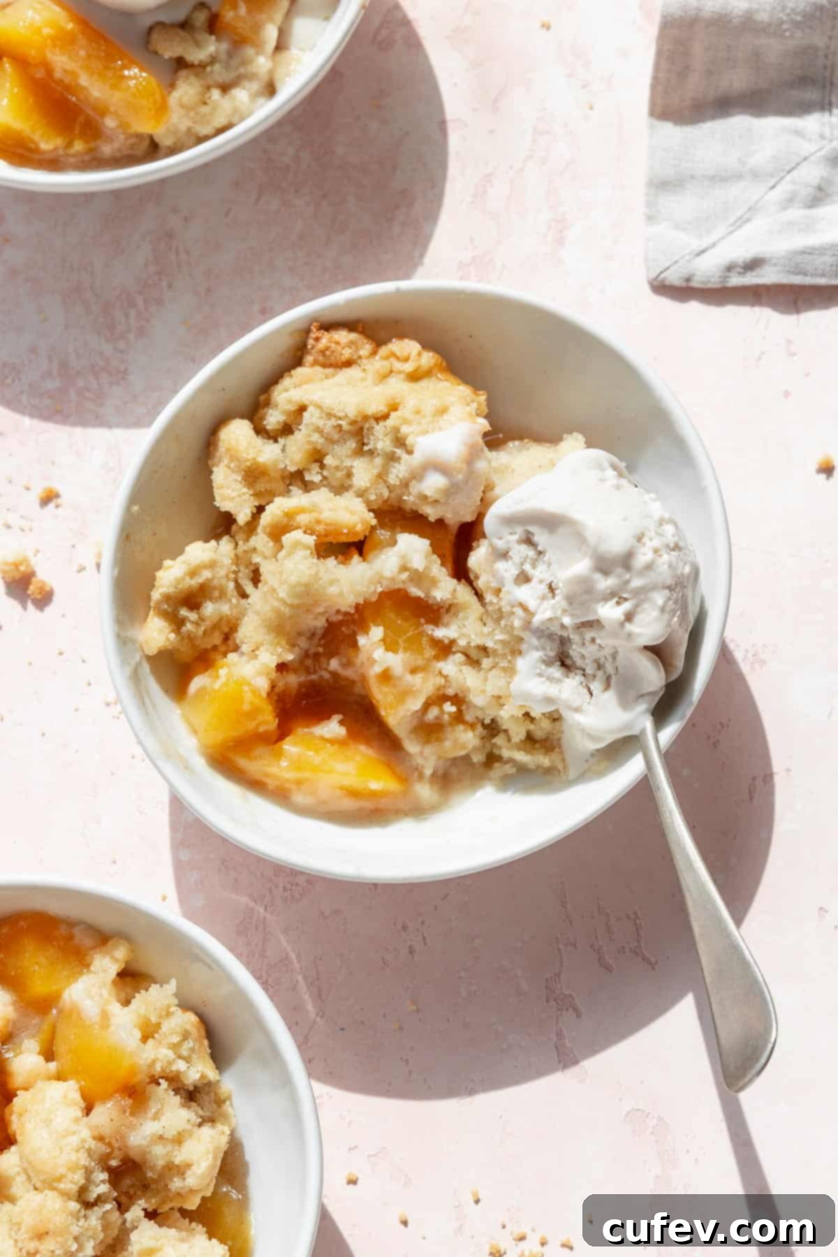 A half eaten bowl of peach cobbler with vanilla ice cream with a spoon in the bowl.