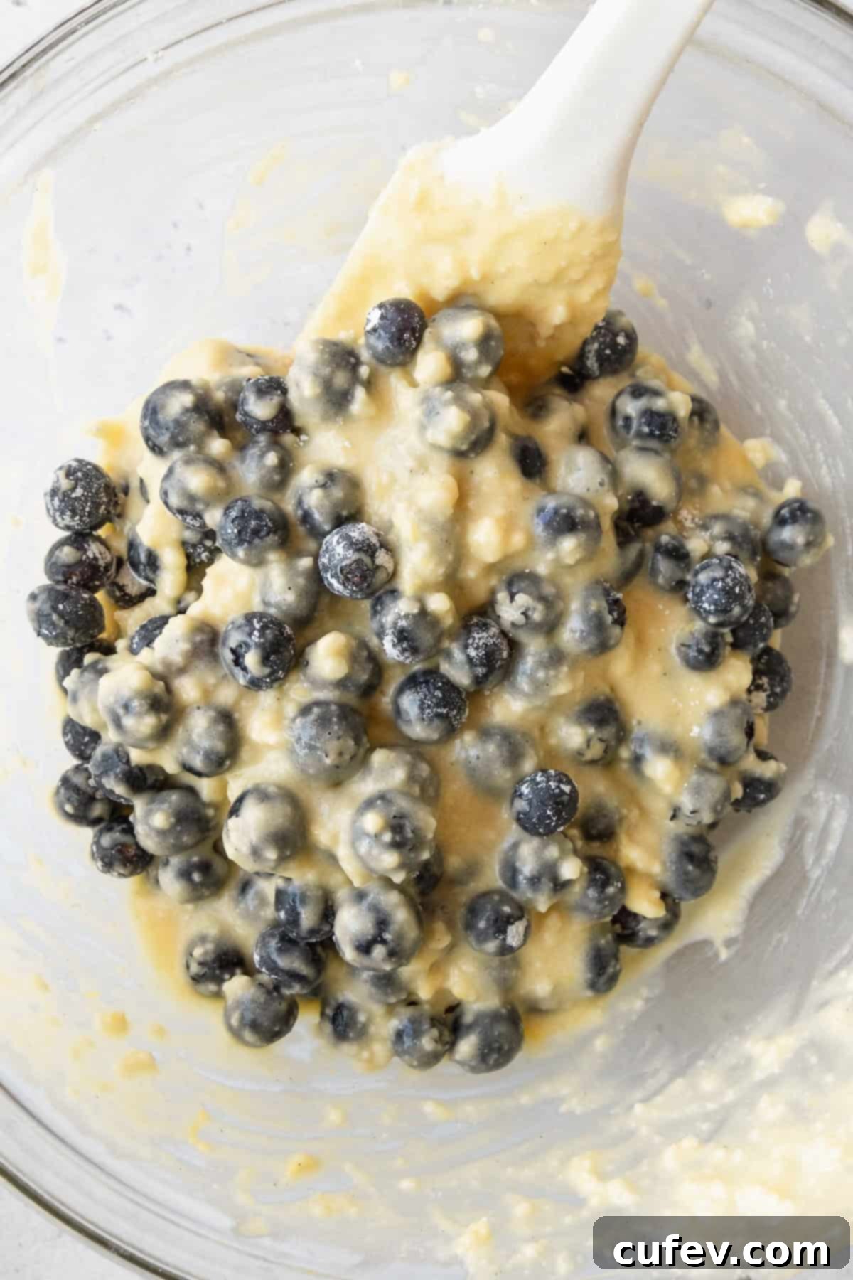 Blueberries being folded into cake batter with a white spatula.
