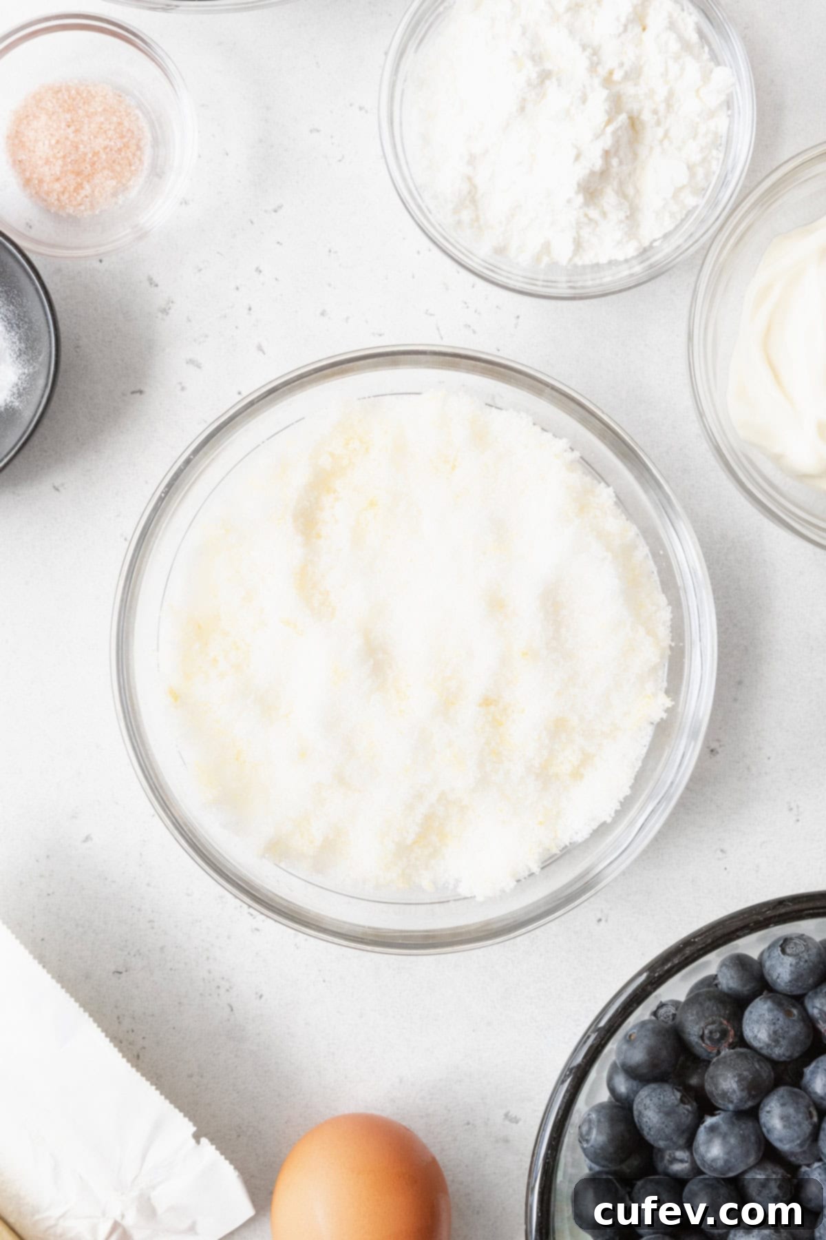 Lemon sugar in a glass bowl, surrounded by more bowls with bake ingredients.